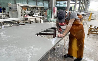 Worker using CNC machine to cut sink hole in white quartz countertop, showing precision fabrication process